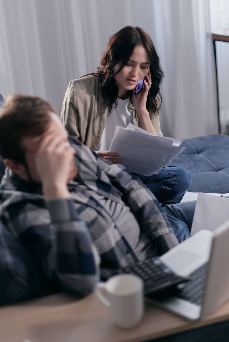 A woman on the phone holding paperwork while another person sits beside her