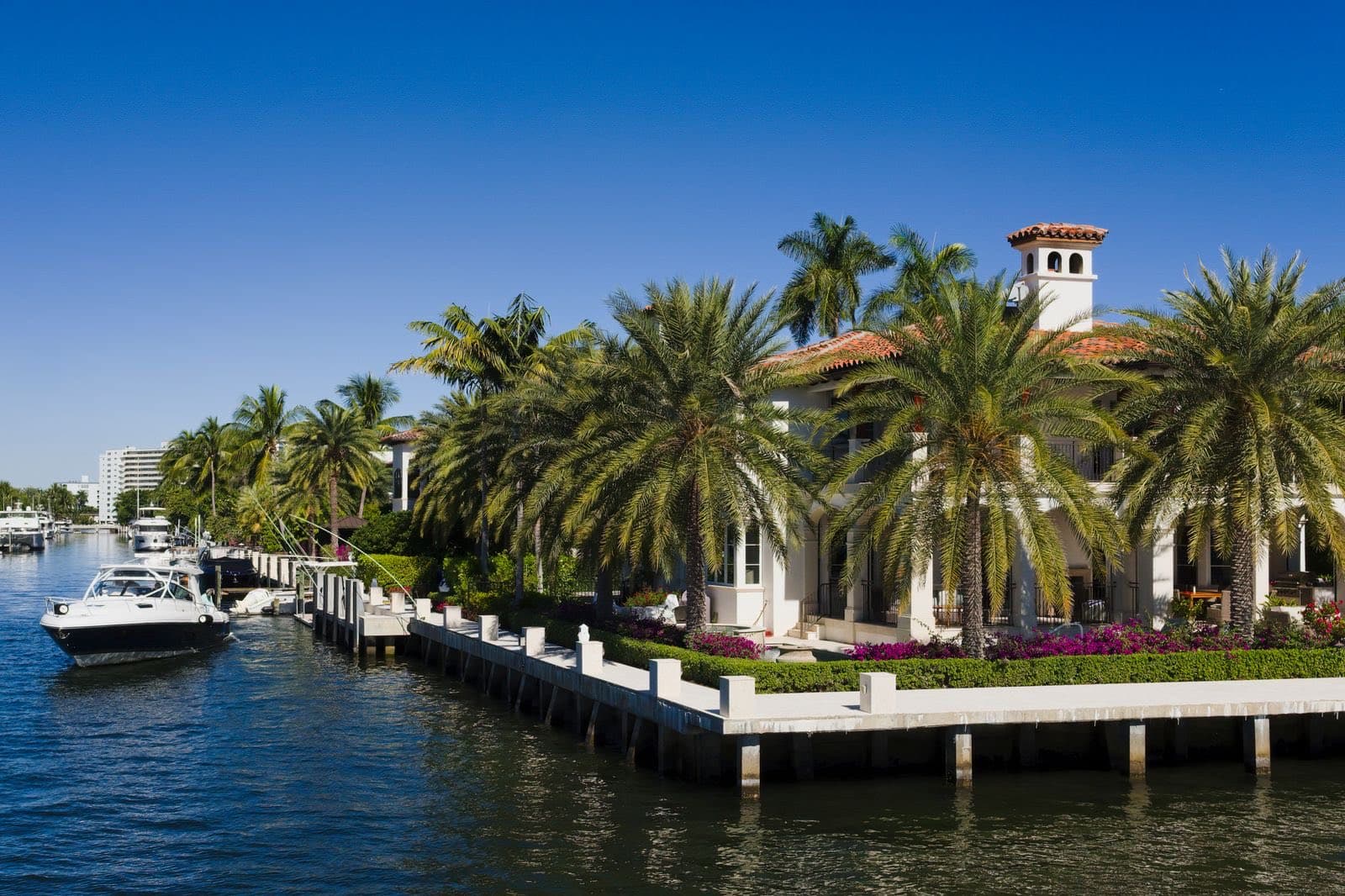 A boat on a Florida canal beside a concrete seawall and waterfront homes with palm trees