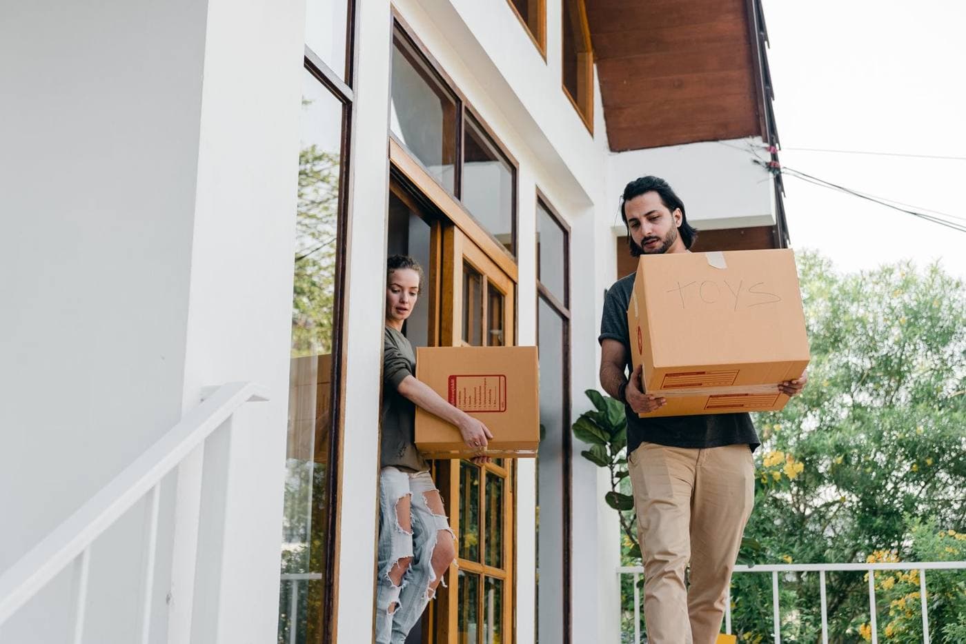 Two people carrying boxes out of a house