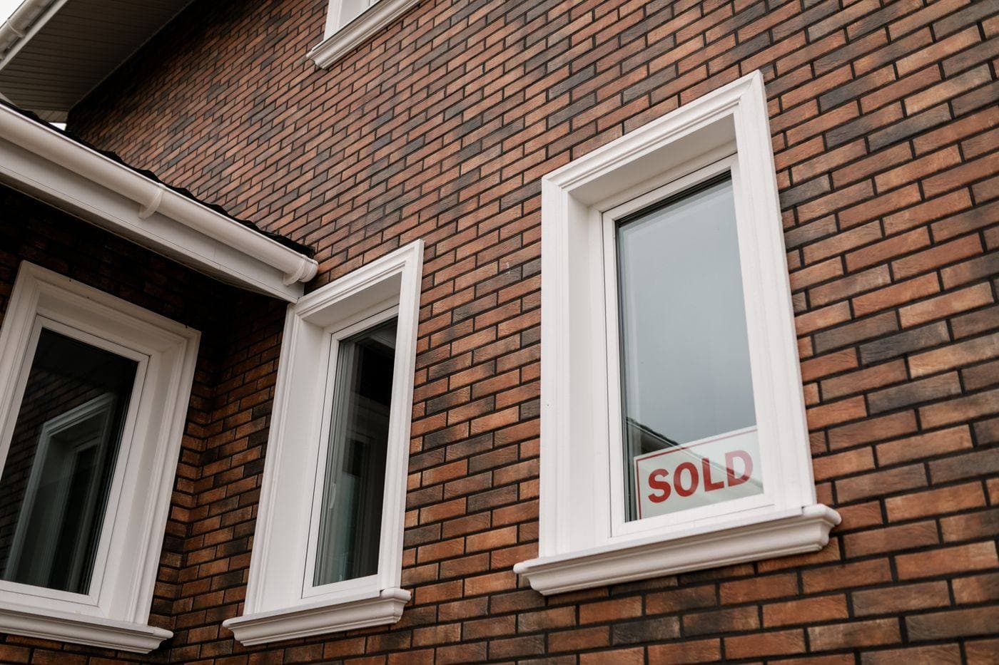 Sold sign in the window of a brick house