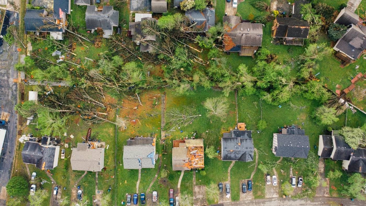 Aerial view of houses with torn roofs and fallen trees after a storm