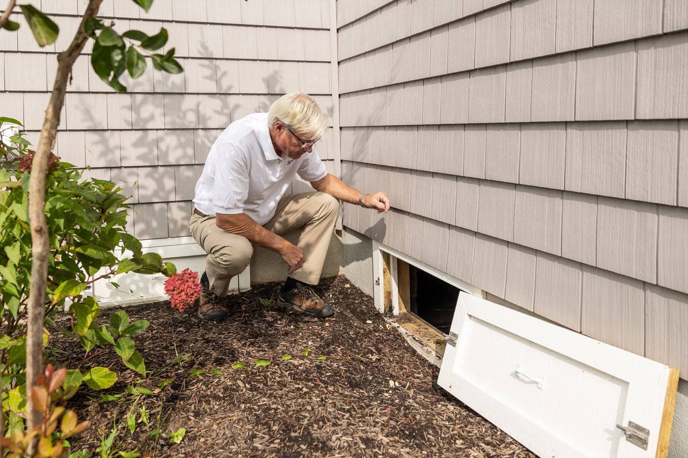 A person examining an opening beneath a house