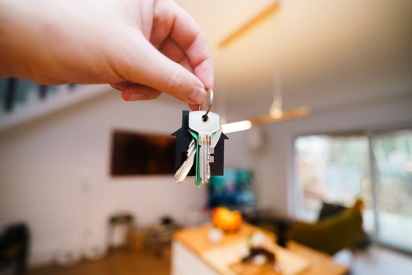 A hand holding house keys in a living room
